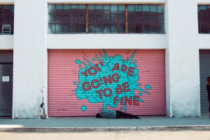 Photo of man lying no ground in front of graffiti that says "you are going to be fine"