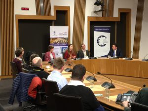 Photo of event with people sitting around a committee room table in the Scottish Parliament