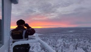 Man with binoculars looks over a large forest covered in snow