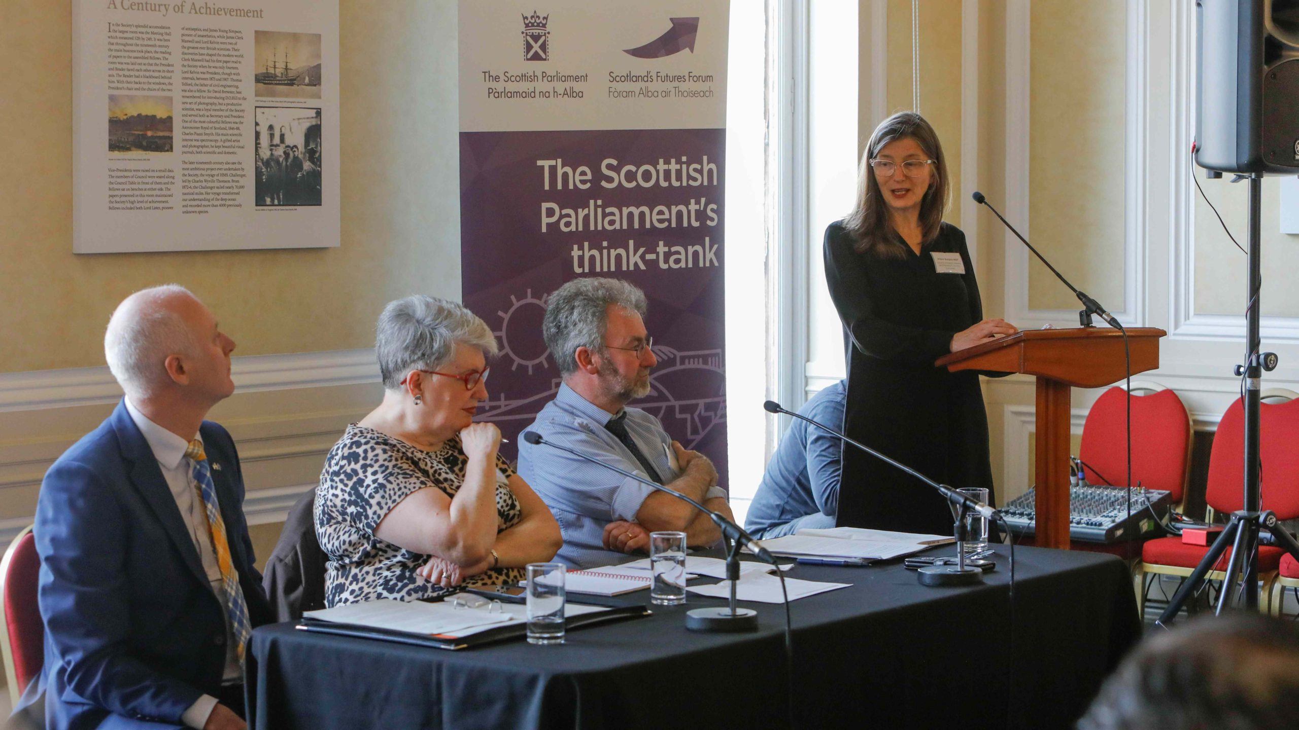 Speaker at a podium next to three people at a table